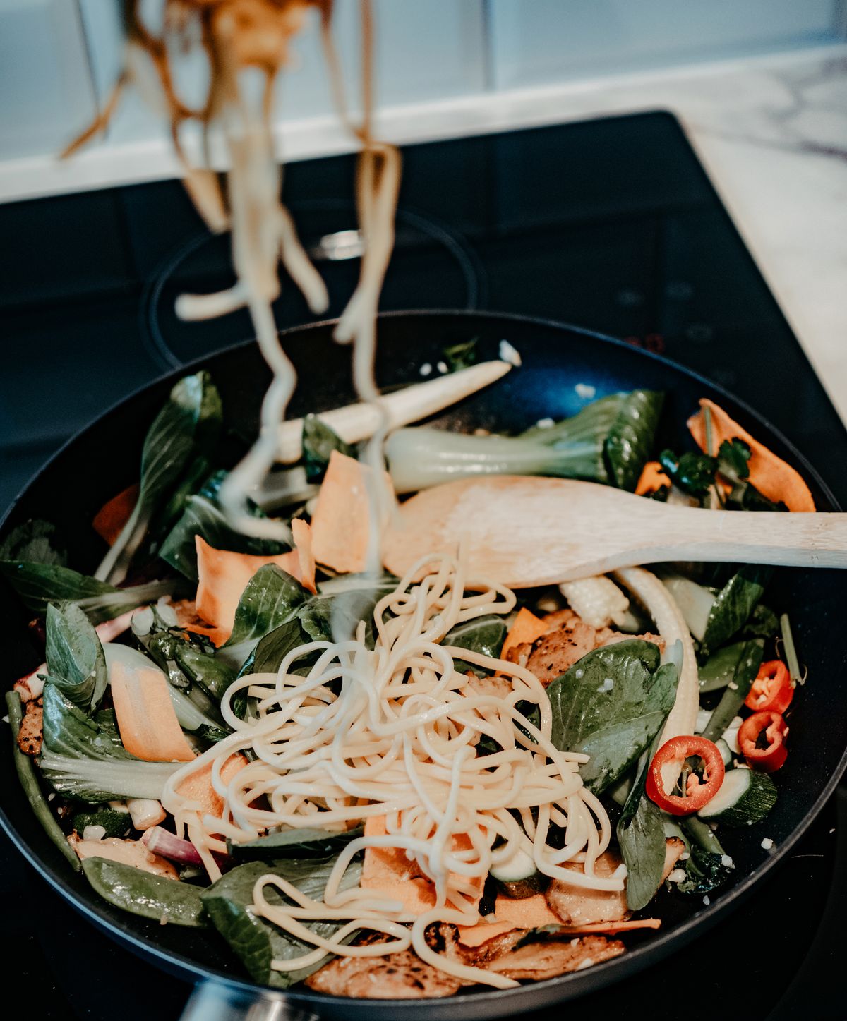 Noodles and vegetables stir-frying in a pan