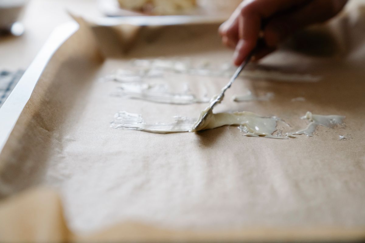 Butter being spread across a lined baking tray